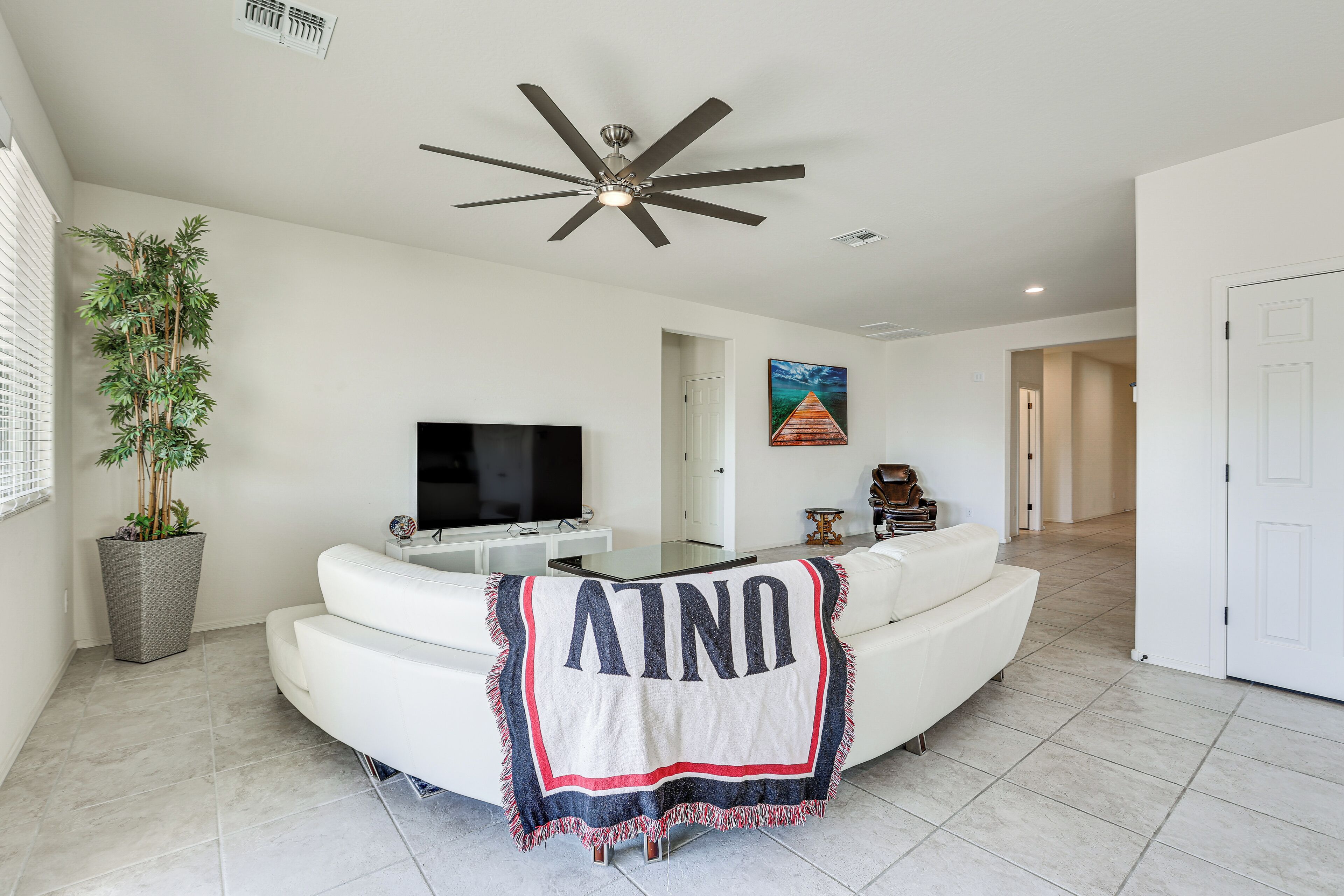 A modern living room with a white sofa, a flat-screen TV, a ceiling fan, and a large potted plant.