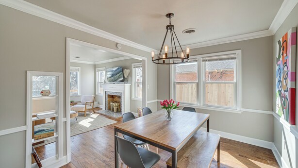 A dining area with a wooden table, chairs, and a chandelier. There is a fireplace in the background, and a window with a view of a wooden deck. - Lovely Tulsa Vacation Rental ~ 3 Mi to Downtown! (Tulsa)