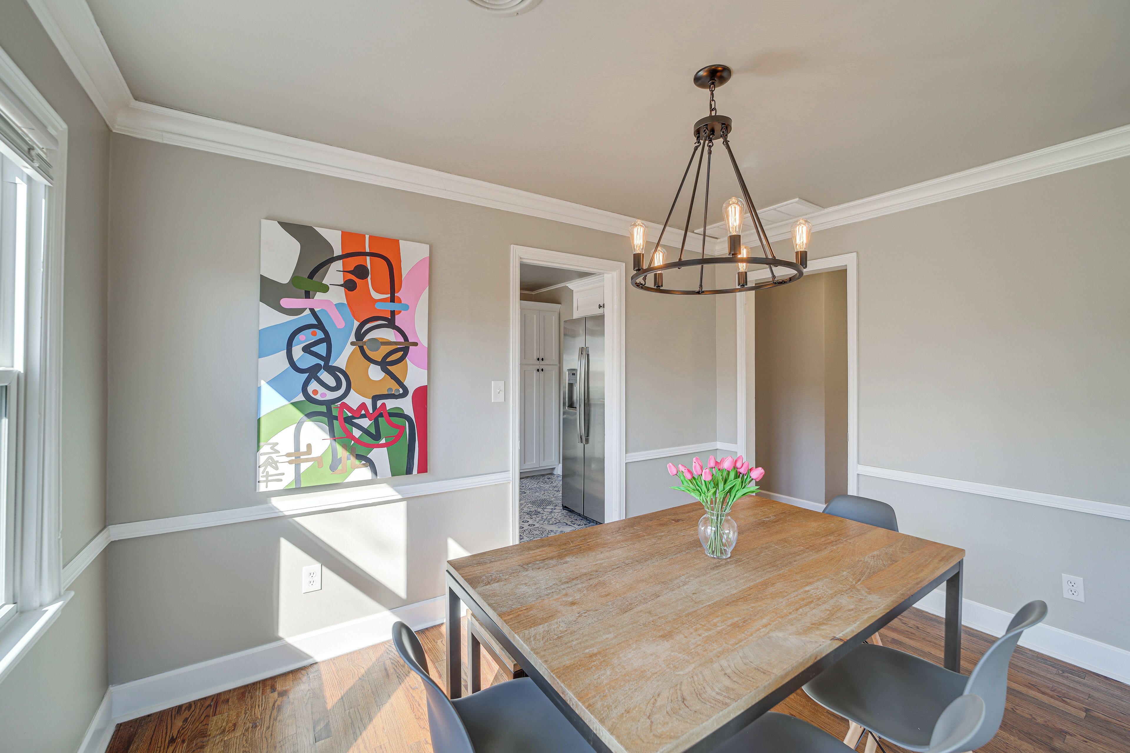 Un coin repas avec une table en bois, des chaises noires, un lustre et un tableau abstrait aux couleurs vives accroché au mur.