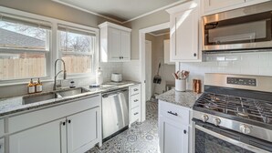 A modern kitchen with white cabinetry, a stainless steel dishwasher, a gas stove, and a large window providing natural light. - Lovely Tulsa Vacation Rental ~ 3 Mi to Downtown! (Tulsa)