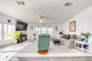 A spacious living room with a green armchair, a sofa, and a TV mounted on the wall.