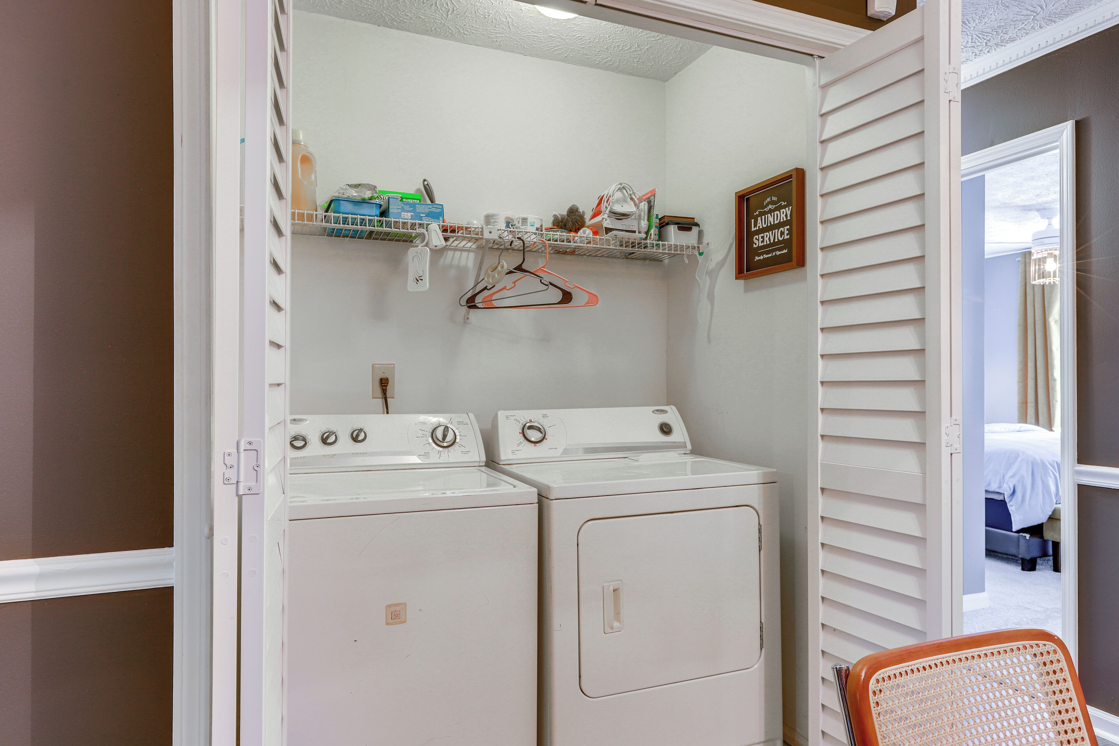 A laundry room with two white washers and dryers, a shelf with laundry supplies, and a sign indicating laundry service.