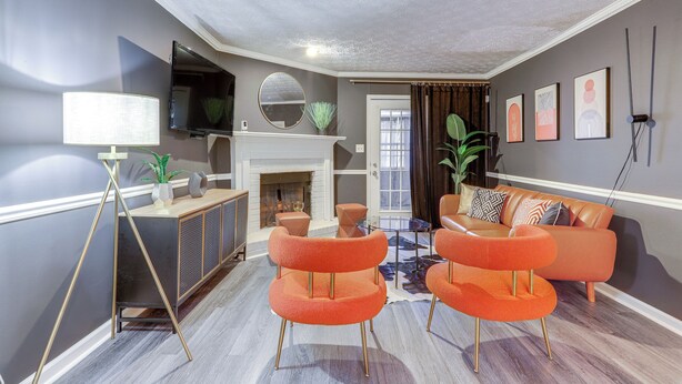 Un salon moderne avec une cheminée, des fauteuils orange, un canapé et un téléviseur fixé au mur.