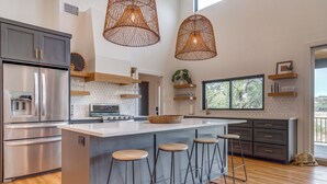 A modern kitchen with a central island, bar stools, stainless steel appliances, and wicker pendant lights.