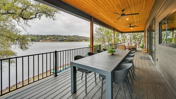 A covered outdoor deck with a table and chairs, overlooking a body of water.