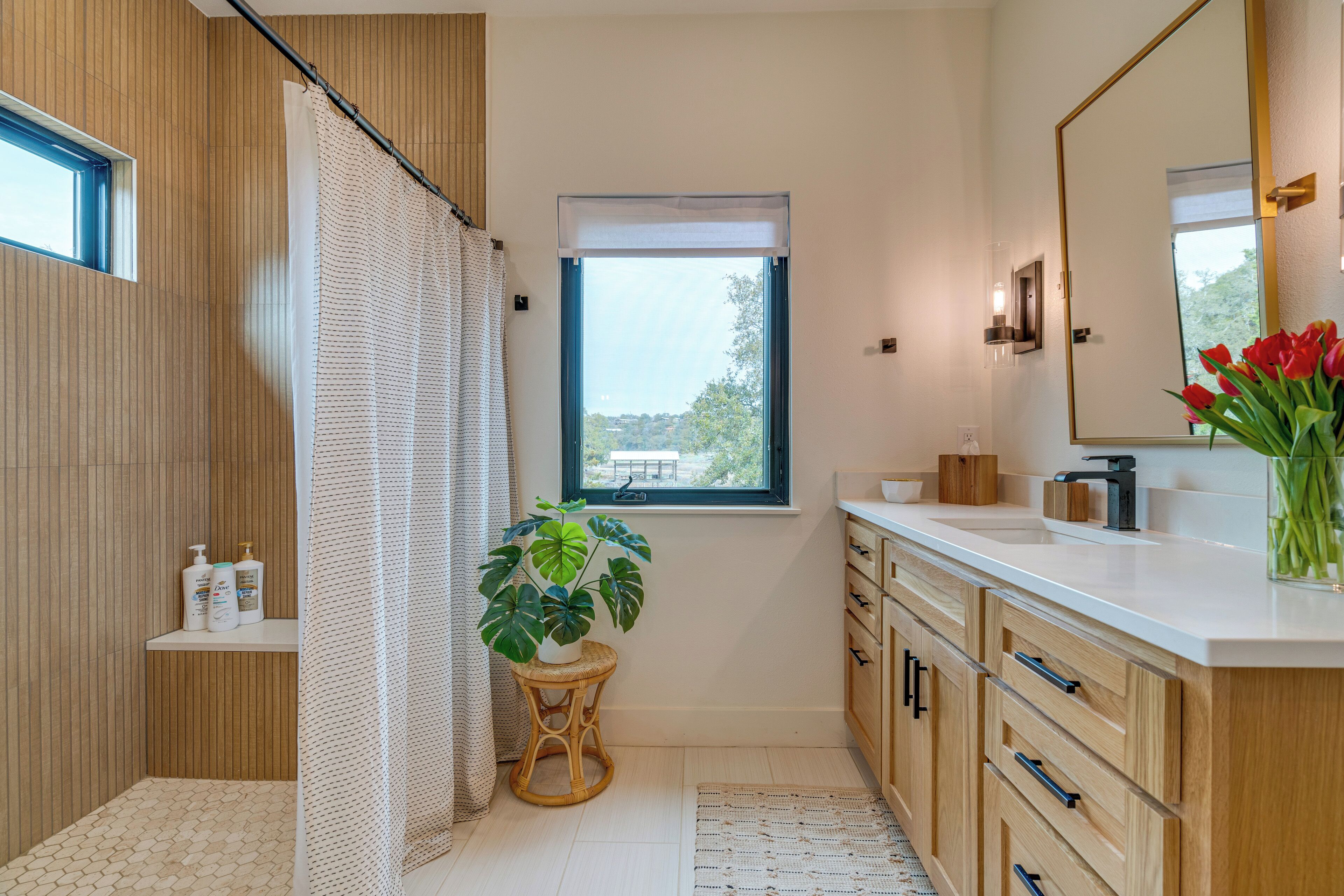 A modern bathroom with wooden paneling, a shower curtain, a window, a sink, a mirror, and a potted plant.