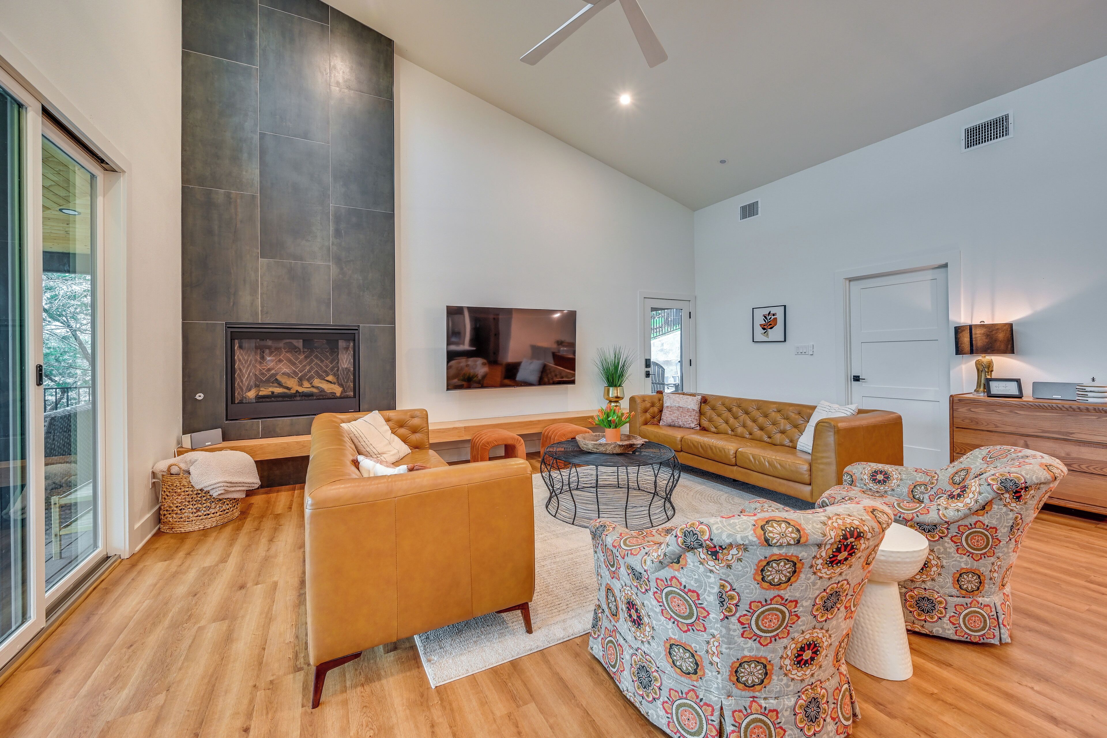 A spacious living room with a fireplace, leather sofas, a coffee table, and a TV mounted on the wall.