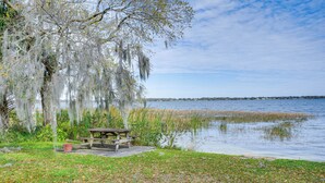 A lakeside picnic area with a wooden bench and a table, surrounded by trees with hanging moss. - Auburndale Vacation Rental w/ Yard & Lake Views (Auburndale)