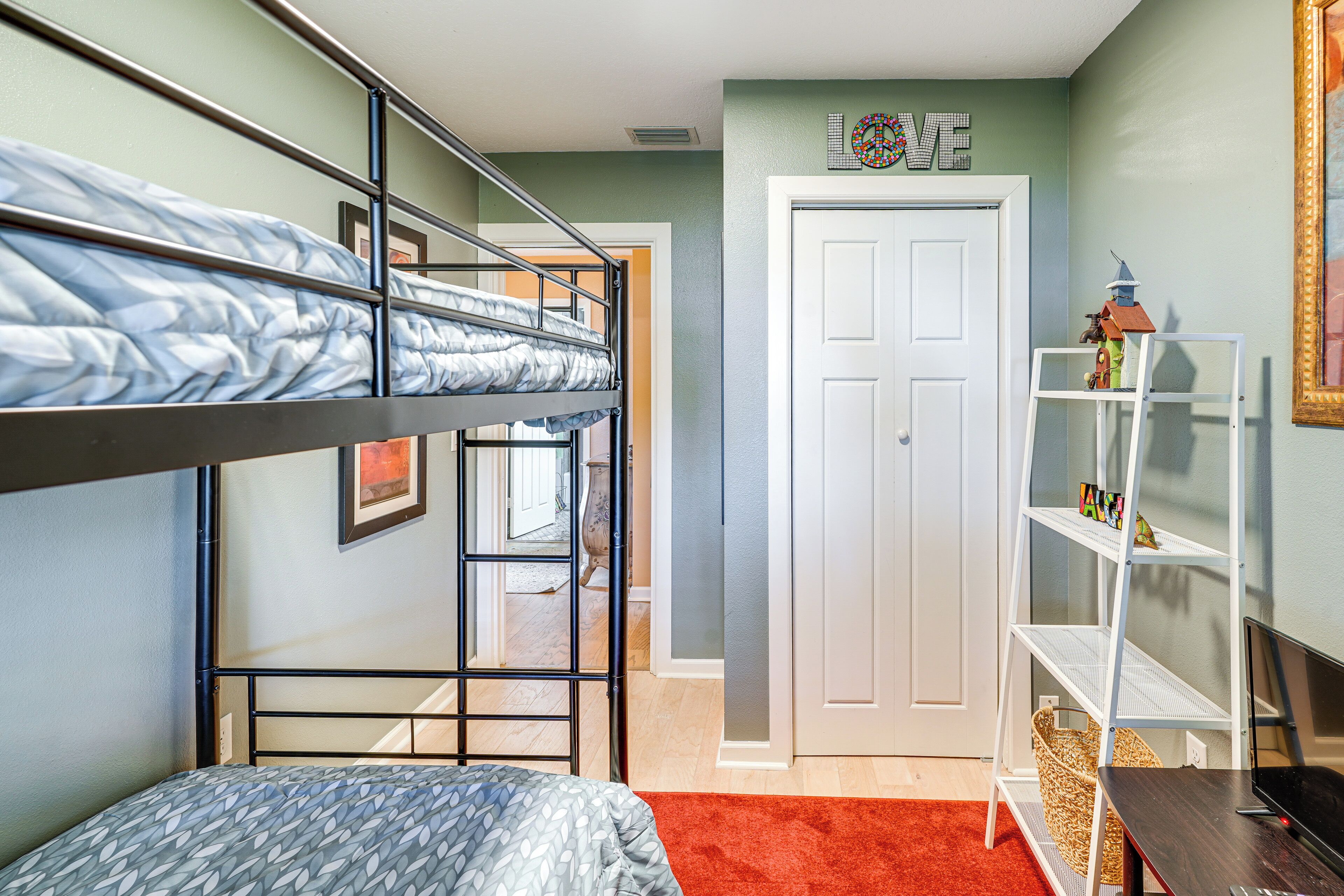 A bunk bed room with a white door, a small white shelf, and a red carpet.