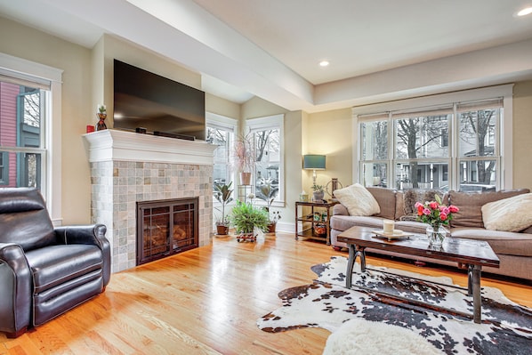A spacious living room with hardwood flooring, a fireplace, a leather recliner, a sofa, and a coffee table.