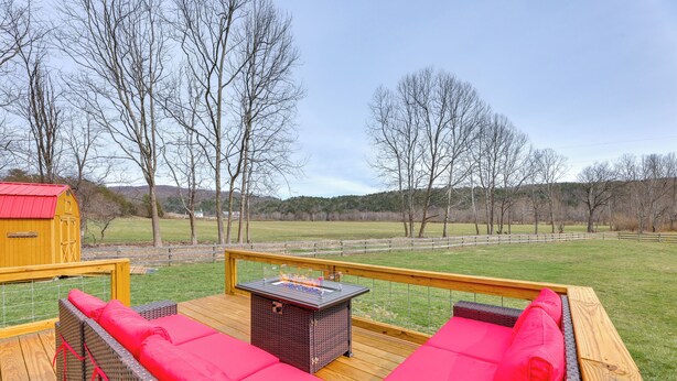 A deck with wicker furniture and red cushions, overlooking a grassy field and trees. - Mcdowell Highland County River Retreat w/ Views! (McDowell)