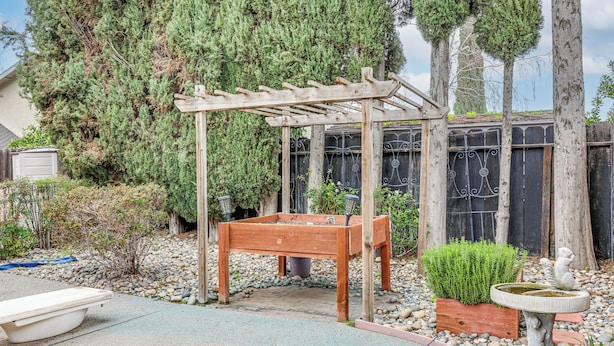 Un jardin agrémenté d’une pergola en bois, d’un parterre surélevé, d’un abreuvoir pour oiseaux et d’une statue.