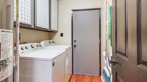 Une buanderie équipée d’un lave-linge et d’un sèche-linge à chargement frontal, avec une porte fermée et un balai appuyé contre le mur.