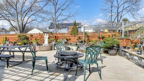 An outdoor patio area with a round table and chairs, surrounded by potted plants and a brick wall. - Spacious Home w/ Tranquil Patio ~ 29 Mi to DC! (Severn)