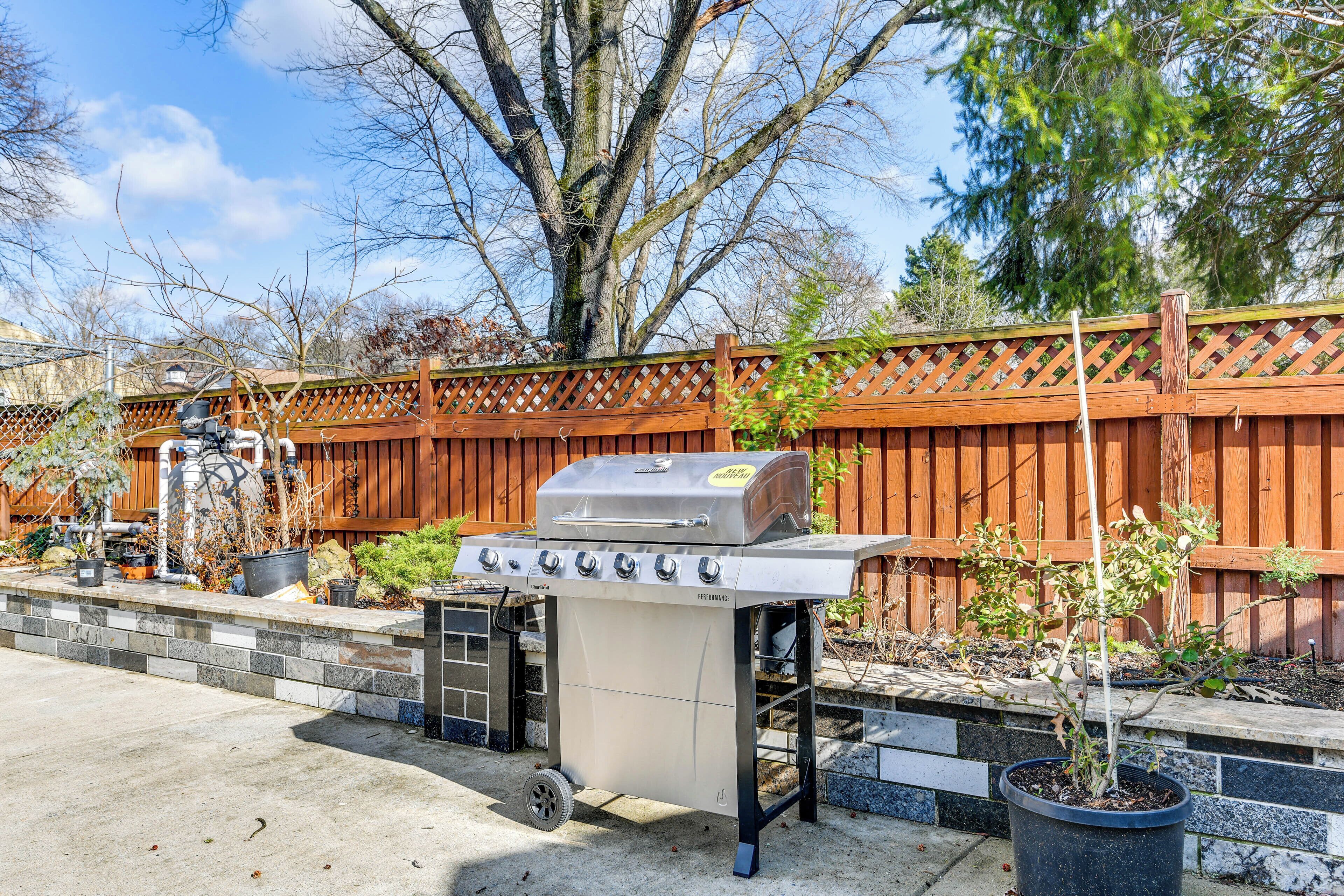 A barbecue grill with a chimney, a stone wall, and a wooden fence in the background.