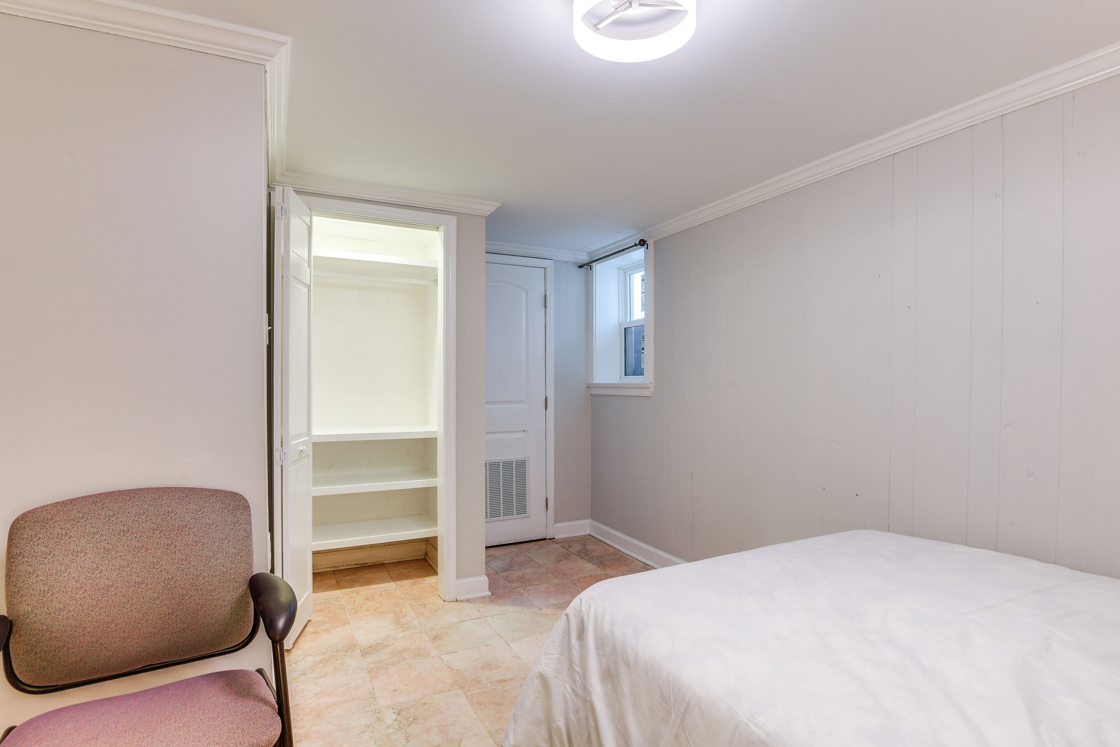 A bedroom with a bed, a chair, a closet, and a window.