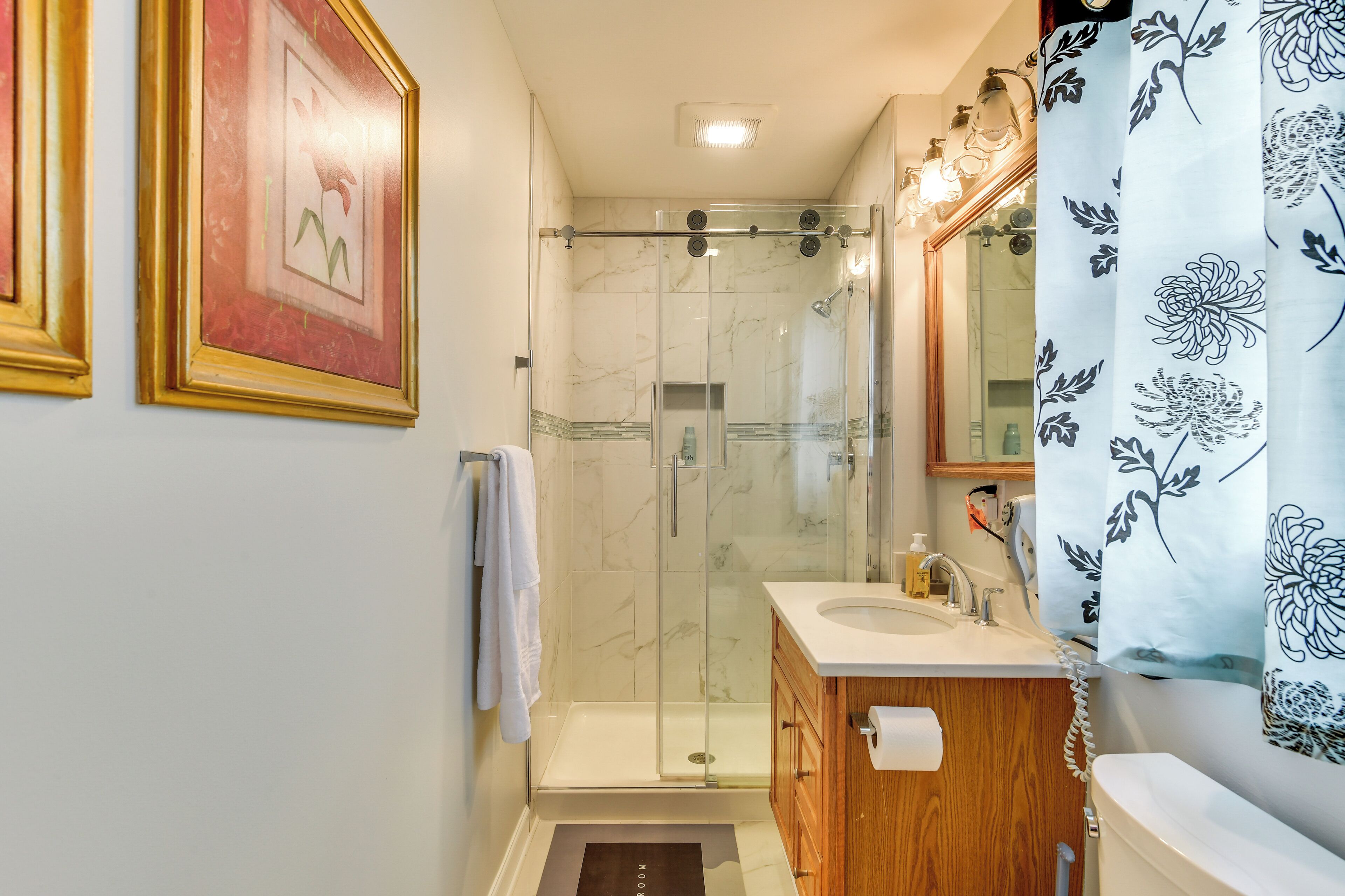 A bathroom with a glass-enclosed shower, a wooden vanity, a marble-tiled wall, and a framed picture.