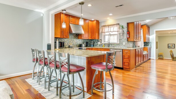 A spacious kitchen with wooden cabinets, a large island with bar stools, and a modern pendant light fixture. - Spacious Home w/ Tranquil Patio ~ 29 Mi to DC! (Severn)