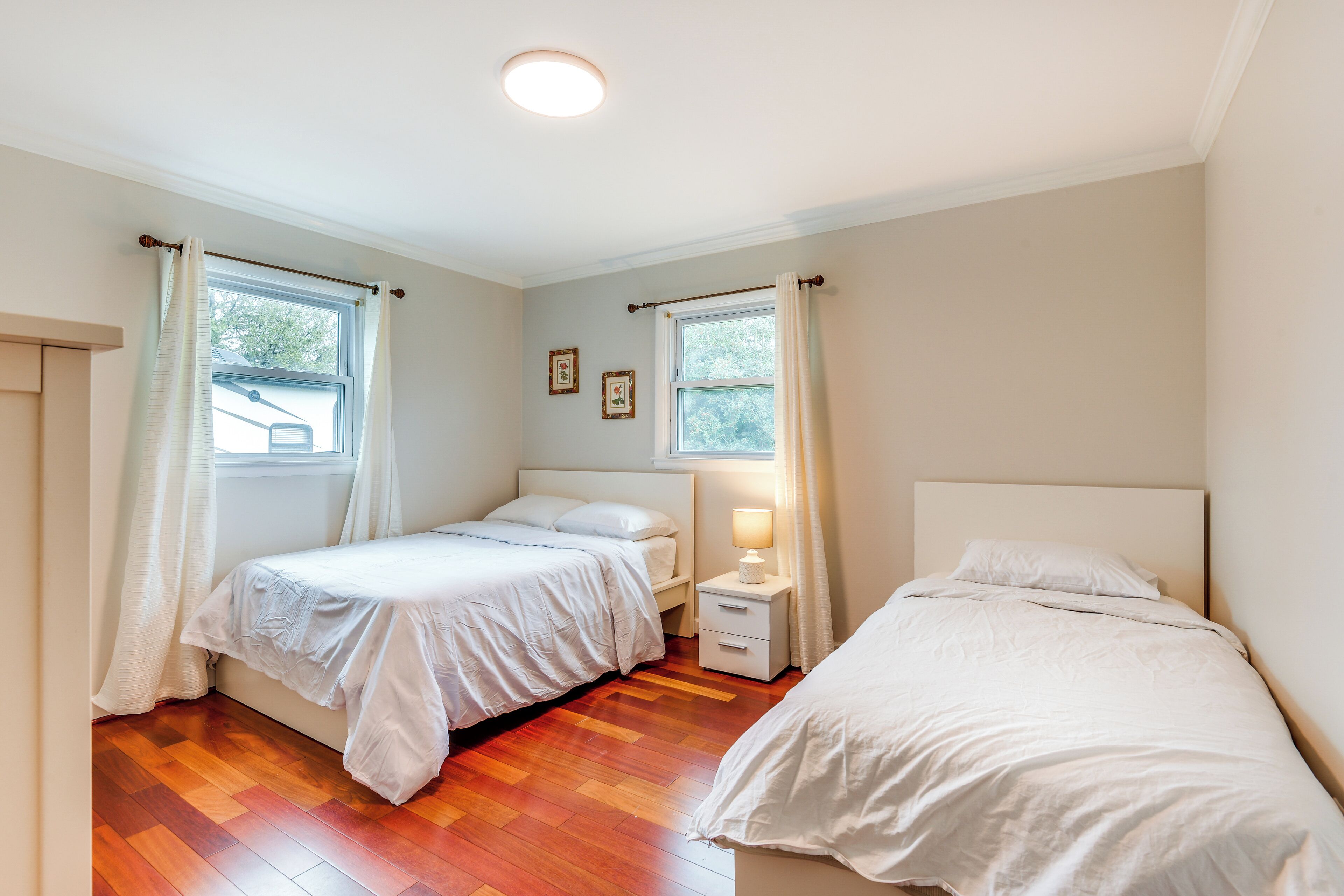 A bedroom with two beds, wooden flooring, and a window with curtains.