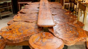 A rustic wooden table with a long central plank and rounded ends, surrounded by matching stools.