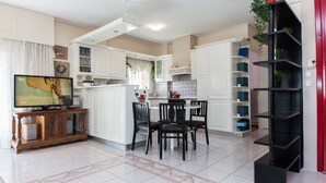 A modern kitchen with white cabinets, a dining area with two chairs, and a TV on a wooden stand. - Classical Beauty 3Bd Apt in Nea Filothei (Athens)