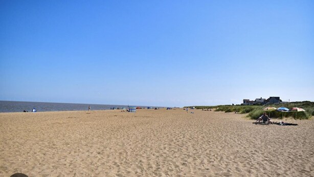 A wide sandy beach with a few umbrellas and tents, a clear sky, and a building in the distance. - Sandy Paws Dog Friendly - Anderby Creek (Skegness)