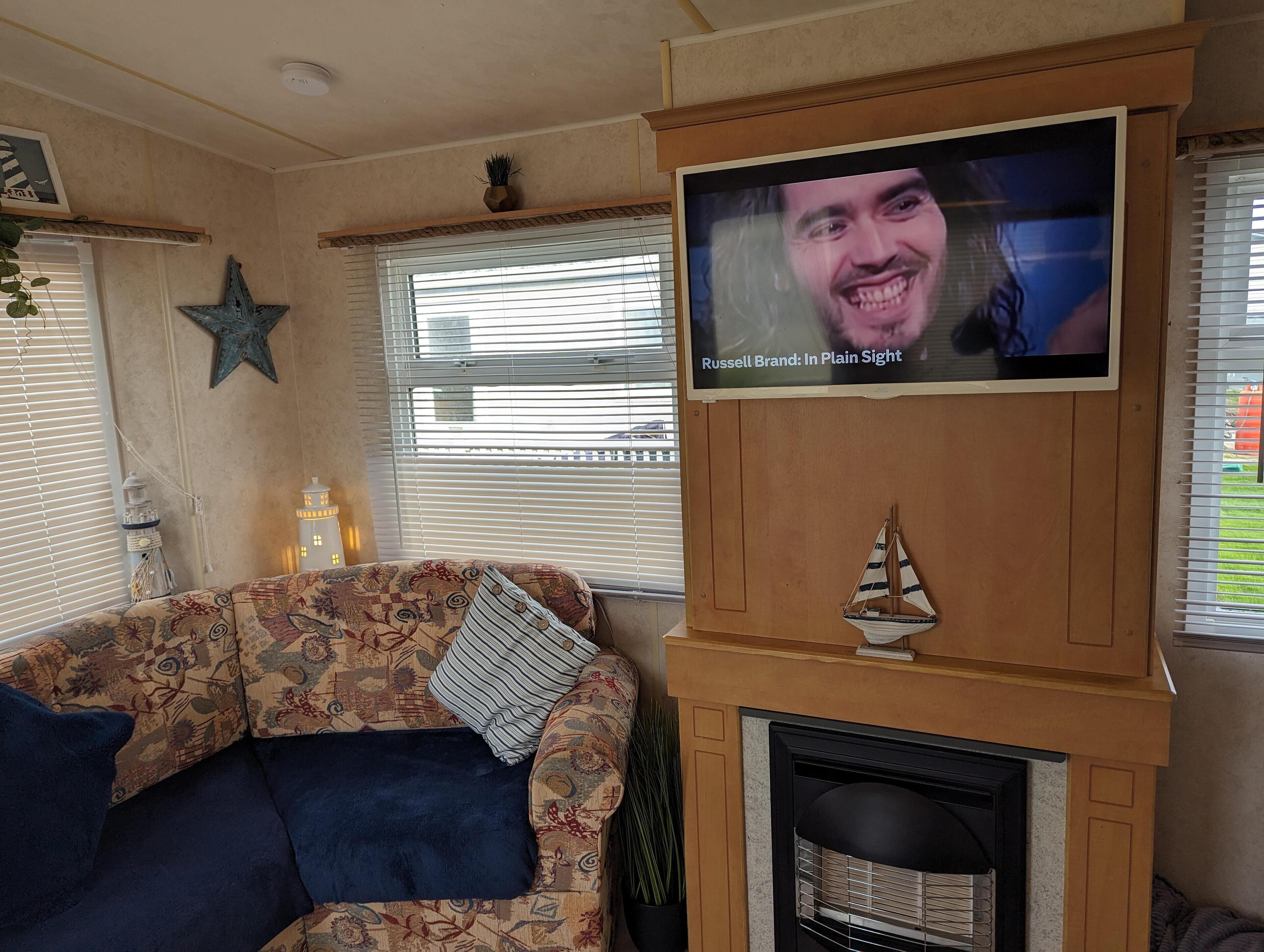 Un salón con un sofá estampado, un televisor montado en una pared de madera, una chimenea y objetos decorativos como una estrella y un barco.