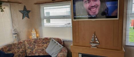 Un salón con un sofá estampado, un televisor montado en una pared de madera, una chimenea y objetos decorativos como una estrella y un barco.