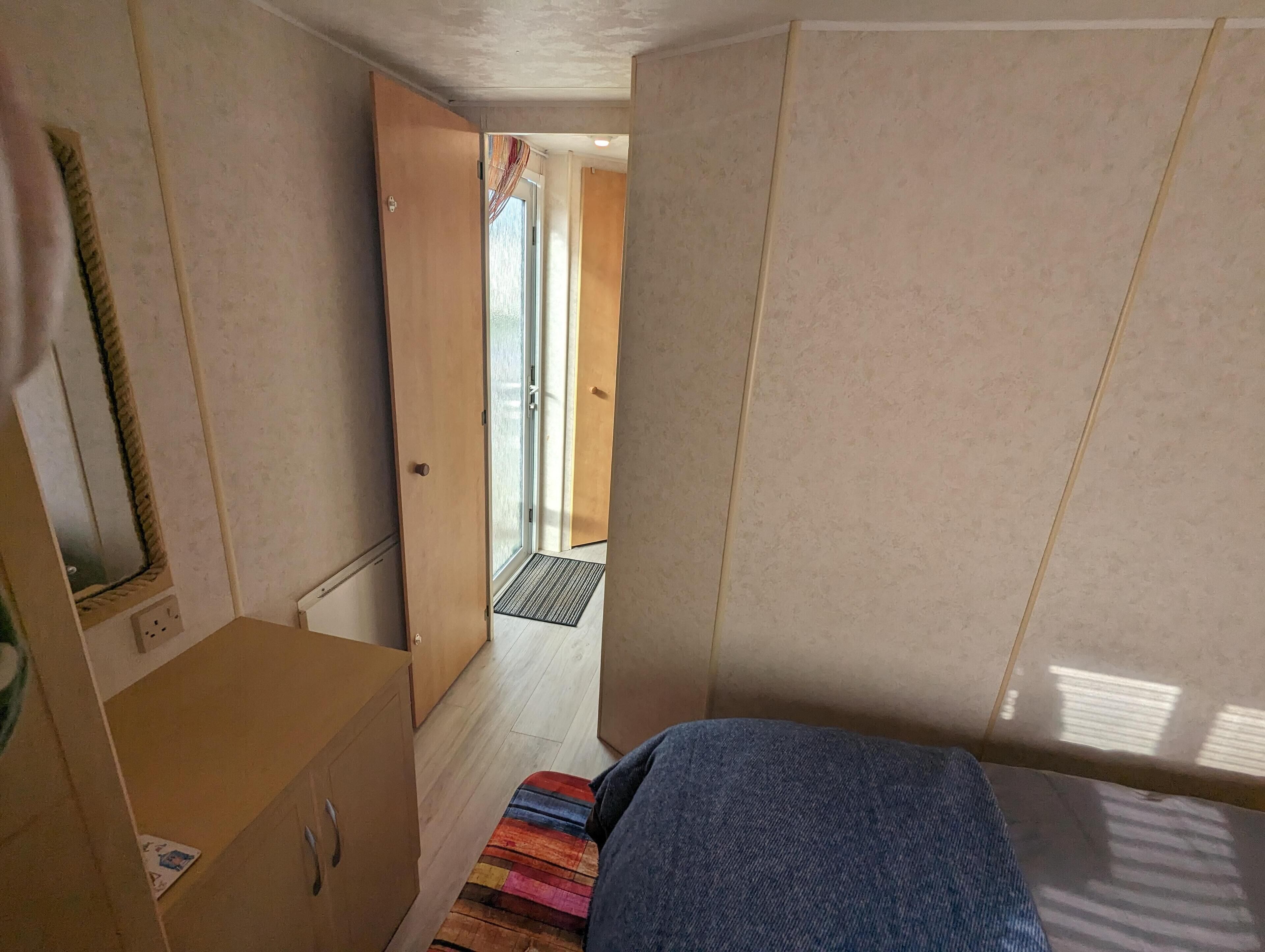 A narrow room with a bed, a wardrobe, and a door leading to a balcony.