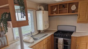 A compact kitchen with a sink, stove, oven, and wooden cabinets. - Sandy Paws Dog Friendly - Anderby Creek (Skegness)