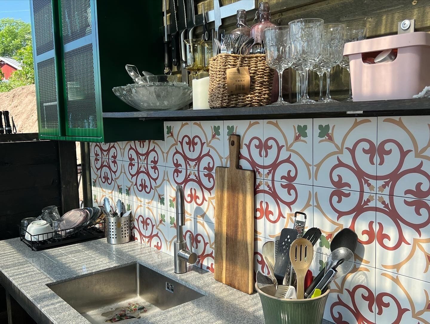 Une cuisine équipée d’un évier, de divers ustensiles, d’une planche à découper et d’un crédence décorative.