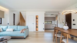 Ein modernes Wohnzimmer mit einer Couch, einem Esstisch mit Stühlen, einer Treppe und einer Küche im Hintergrund.