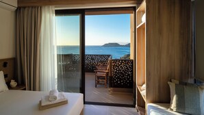 Ein Hotelzimmer mit Bett, einem kleinen Tisch mit Handtuch, einem Balkon mit Stuhl und Blick aufs Meer.