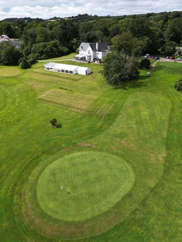 Un campo de golf amplio y bien cuidado, con un club de campo y una zona cubierta con carpas.
