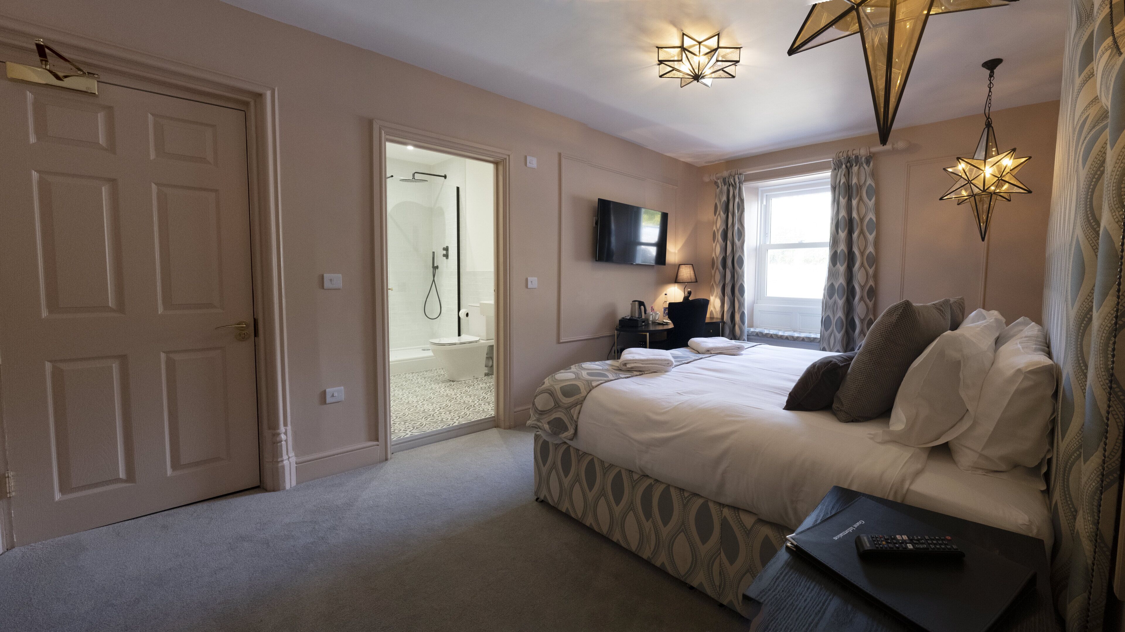 A bedroom with a bed, a TV, a bedside table, a lamp, and a window with curtains.