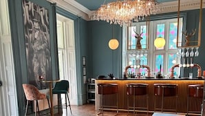 A bar area with a wooden bar counter, multiple stools, a chandelier, and a large window with colorful glass panes. - Welbeck Manor and Golf  (Plymouth)
