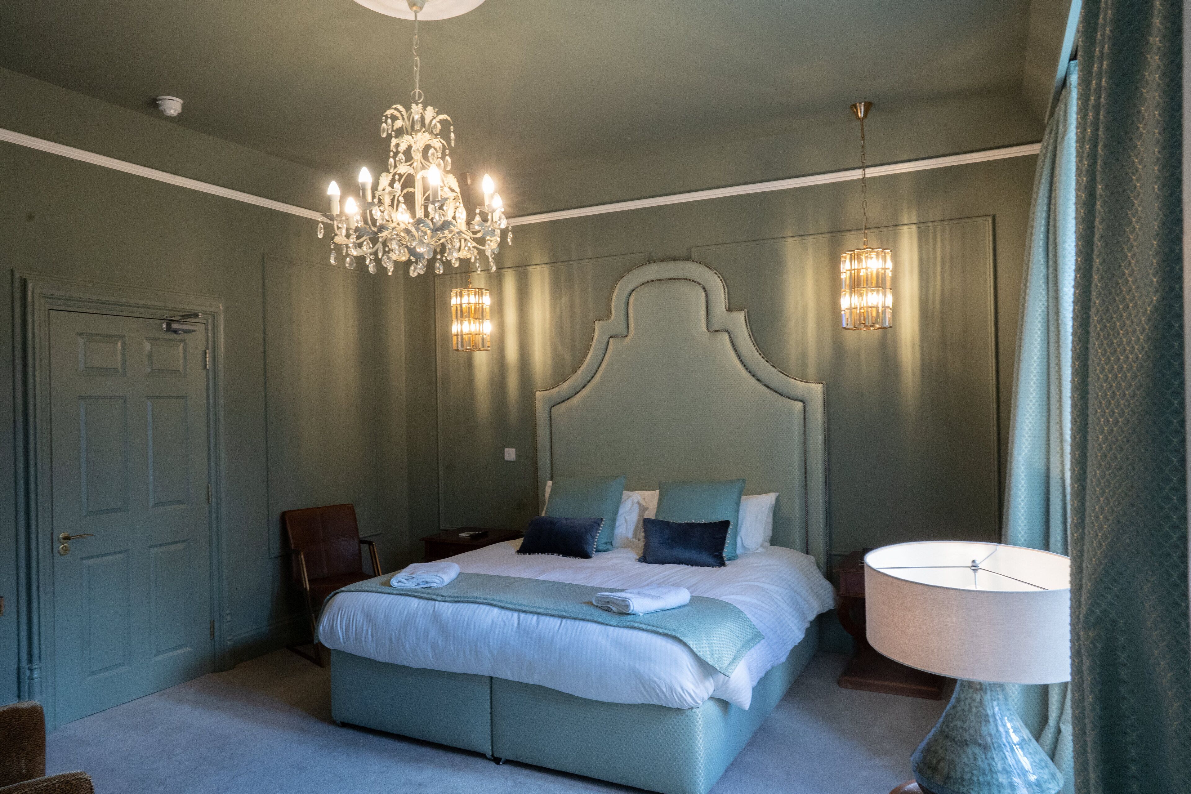 A bedroom with a large bed, a chandelier, bedside lamps, and a door.