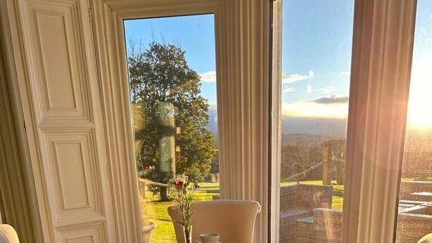 A dining area with a round table, four chairs, and a view of a garden and building through large windows. - Welbeck Manor and Golf  (Plymouth)