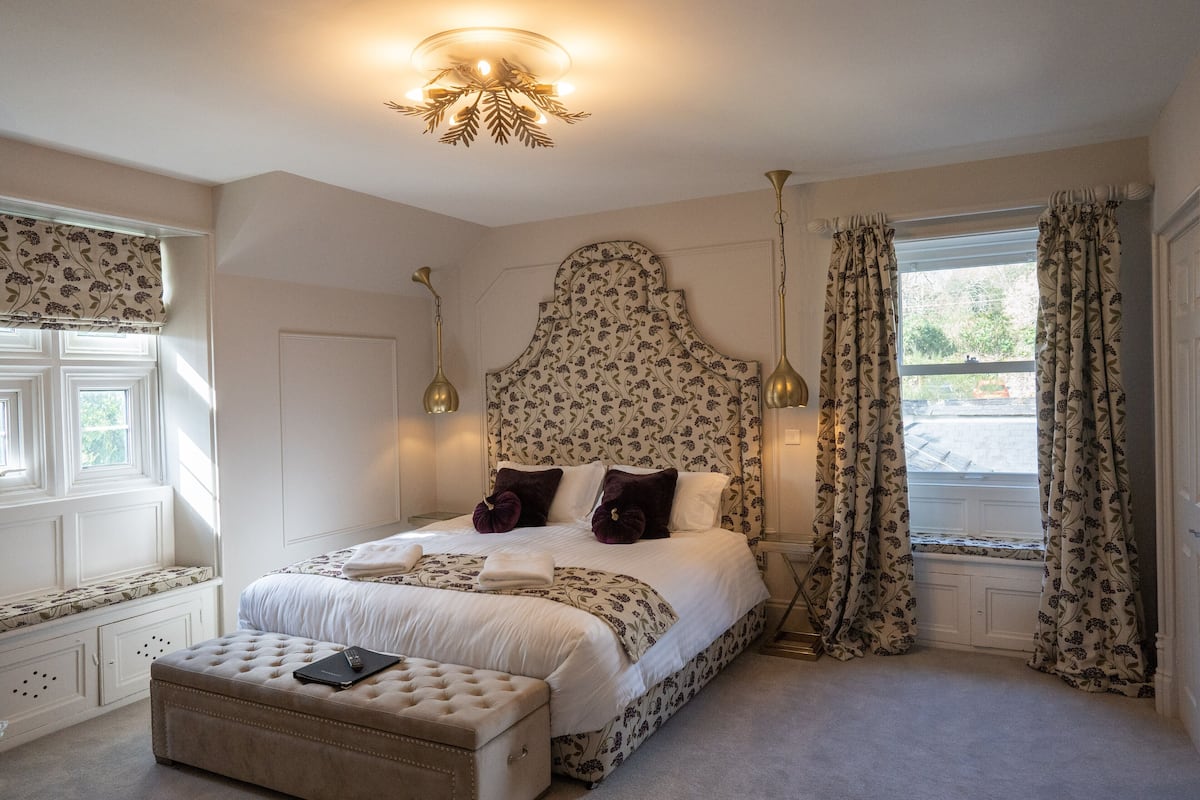 A bedroom with a large bed, a bedside table, a window with curtains, and a ceiling light fixture.