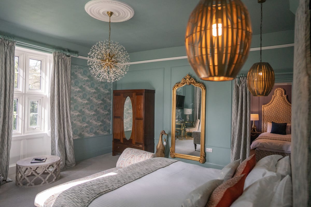 A bedroom with a large bed, a round side table, a mirror, and a wardrobe.