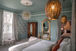 A bedroom with a large bed, a round side table, a mirror, and a wardrobe.