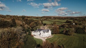 A large, white, two-story house with a symmetrical roof and multiple chimneys, surrounded by lush green fields and scattered trees. - Welbeck Manor and Golf  (Plymouth)