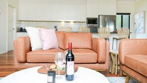 A modern living room with a sofa, a table with a bottle of wine, glasses, and snacks. - 113 Barrage Rd Goolwa South (Goolwa South)