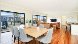 A spacious living area with a wooden dining table, grey upholstered chairs, a brown sofa, and a television. - 113 Barrage Rd Goolwa South (Goolwa South)