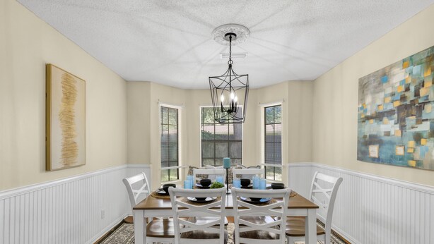A dining room with a wooden table, white chairs, a chandelier, and artwork on the walls. - 3Br, 2Ba, 6 beds, 5 min from Fort Novosel (Daleville)