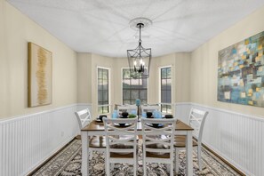 A dining room with a wooden table, white chairs, a chandelier, and artwork on the walls.