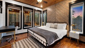 Ein Schlafzimmer mit einem Bett, einem Schreibtisch und einem Sessel. Es gibt große Fenster und einen Deckenventilator.