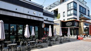 Ein Straßen-Café mit Tischen, Stühlen, Sonnenschirmen und einem Gebäude mit der Beschriftung "ZAZA GELATO".