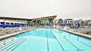 Ein Swimmingpool mit blauen Sonnenschirmen und Liegestühlen, umgeben von modernen Gebäuden.
