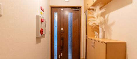 A hallway with a wooden door, a fire alarm, and a cabinet with a decorative item.